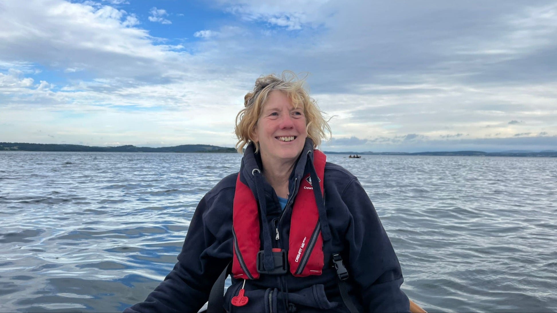 Person on a boat wearing a red life jacket with a scenic background of water and sky.